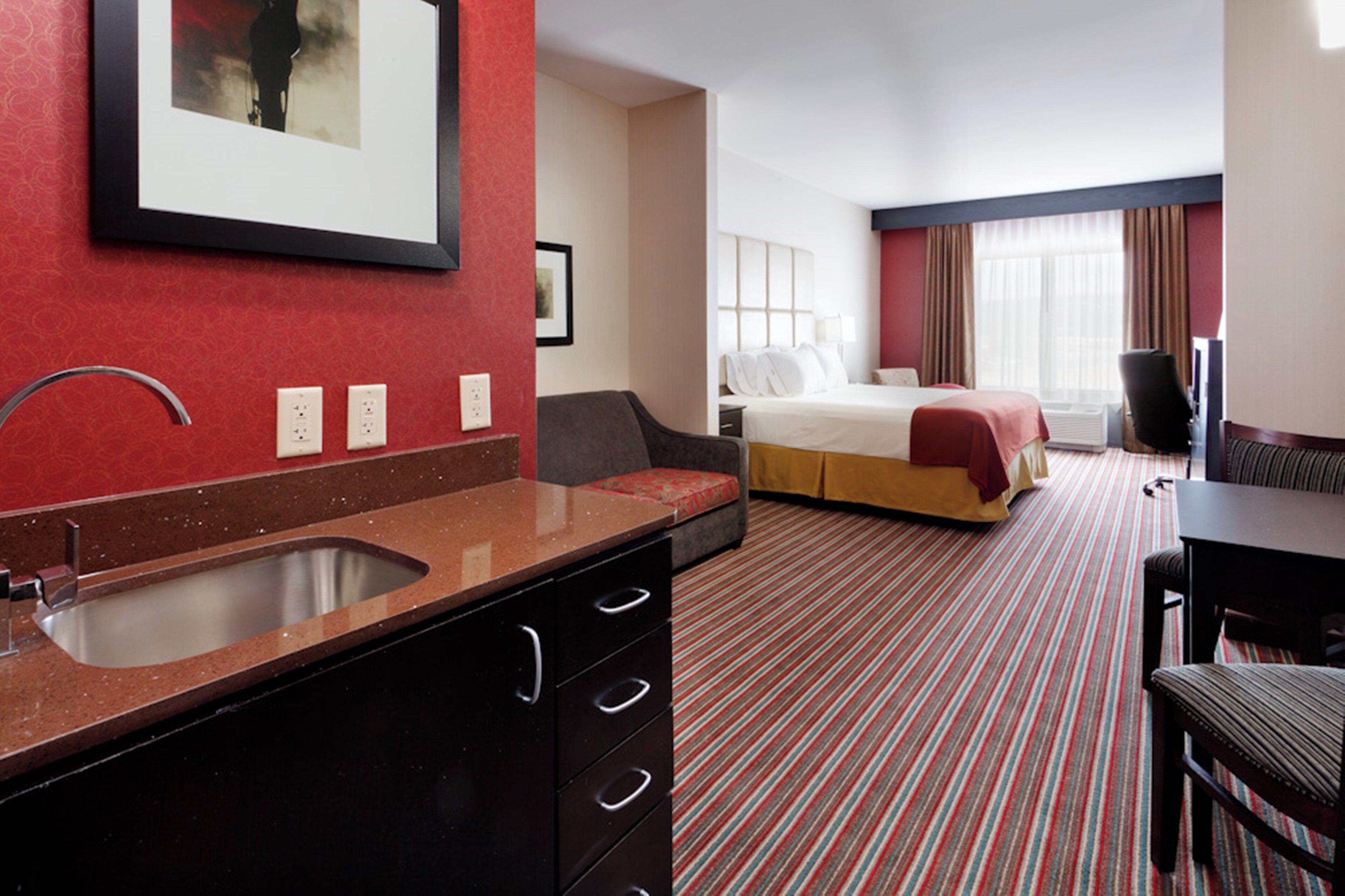 Una habitación de hotel con cama, escritorio, silla, lavabo y espejo.
