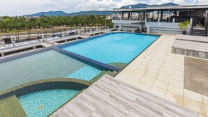 A large outdoor swimming pool with a view of mountains and a building in the background. - Malin Patong Hotel (Patong)