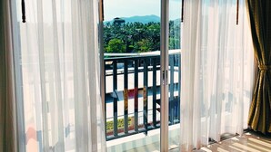 A room with a large sliding glass door leading to a balcony with a view of greenery and mountains. - Malin Patong Hotel (Patong)
