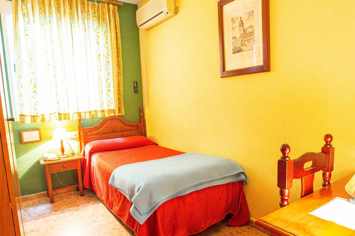 Quarto com duas camas, uma mesa de cabeceira de madeira, uma mesa, uma cadeira, um quadro na parede e um ar condicionado.
