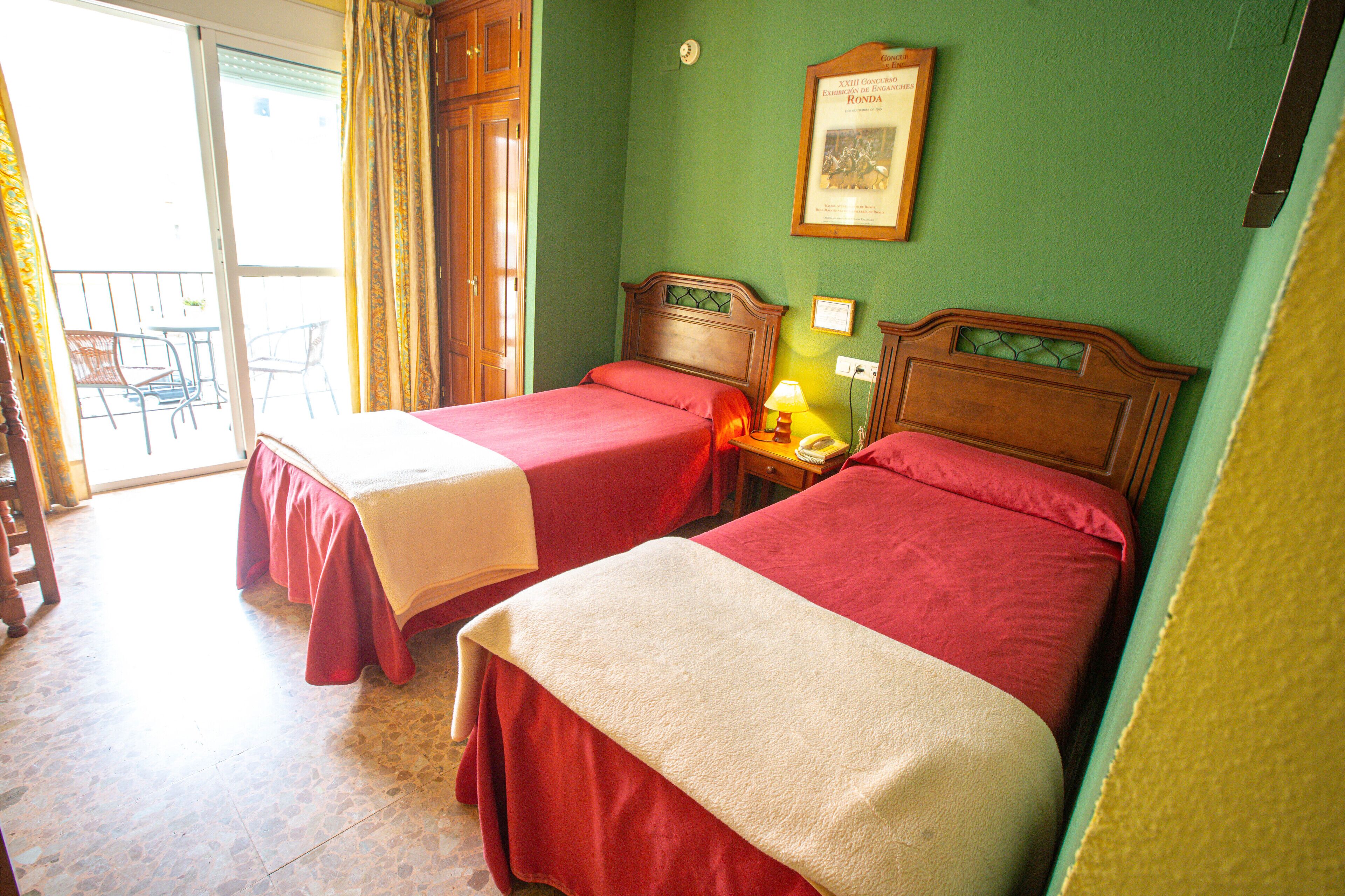 Een hotelkamer met twee bedden, een balkon met stoelen en een ingelijst certificaat aan de muur.