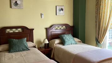 A hotel room with two beds, a nightstand with a lamp, an air conditioning unit, and two wall-mounted paintings.