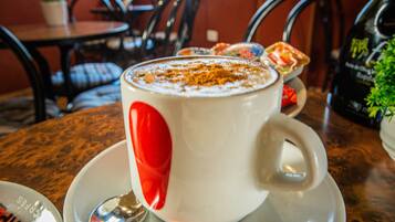 Una taza blanca con un diseño de corazón rojo sobre un platito, sobre una mesa con una cuchara y un sobre de leche para café.
