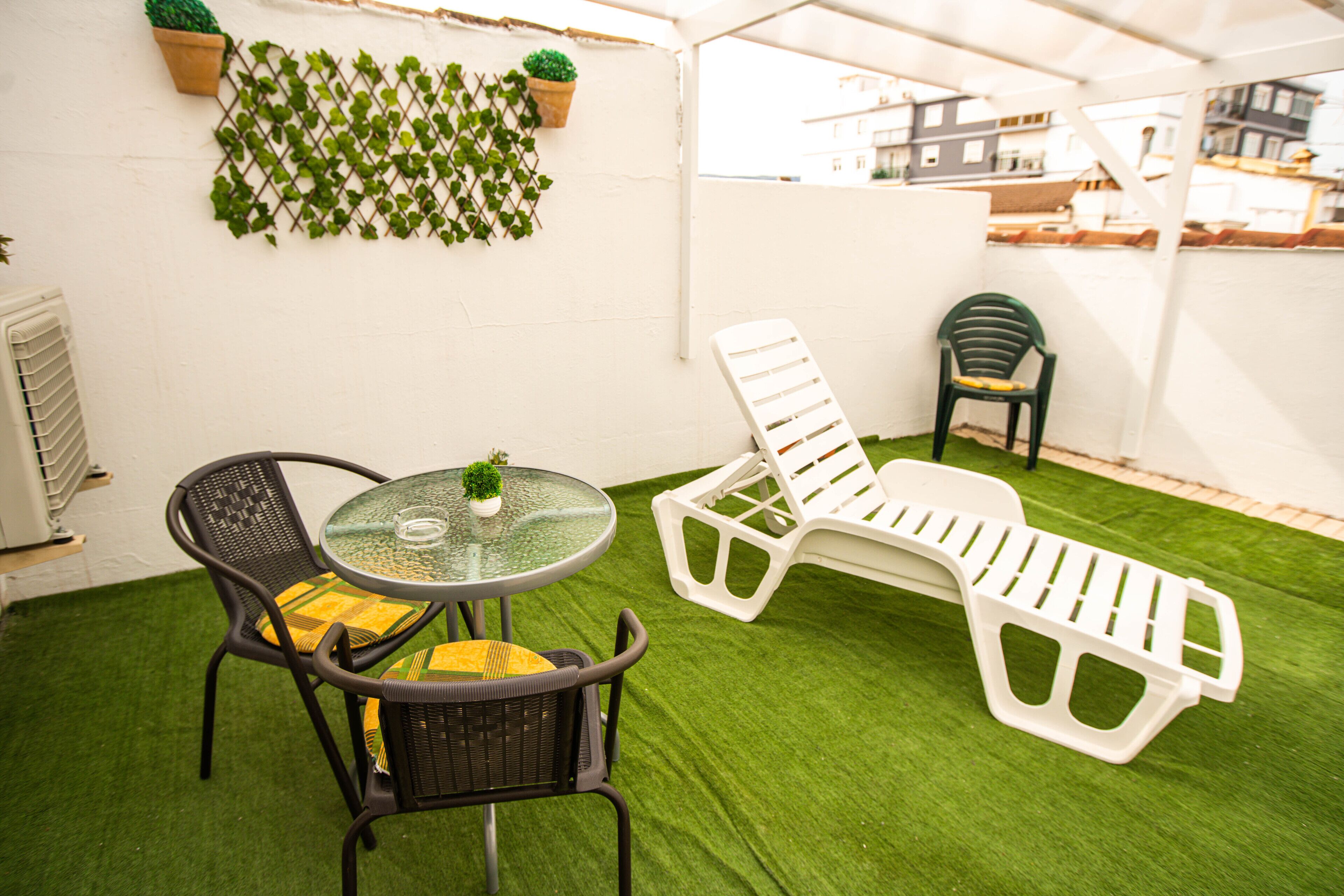 Un patio con una mesa redonda, dos sillones de descanso y una planta en maceta.