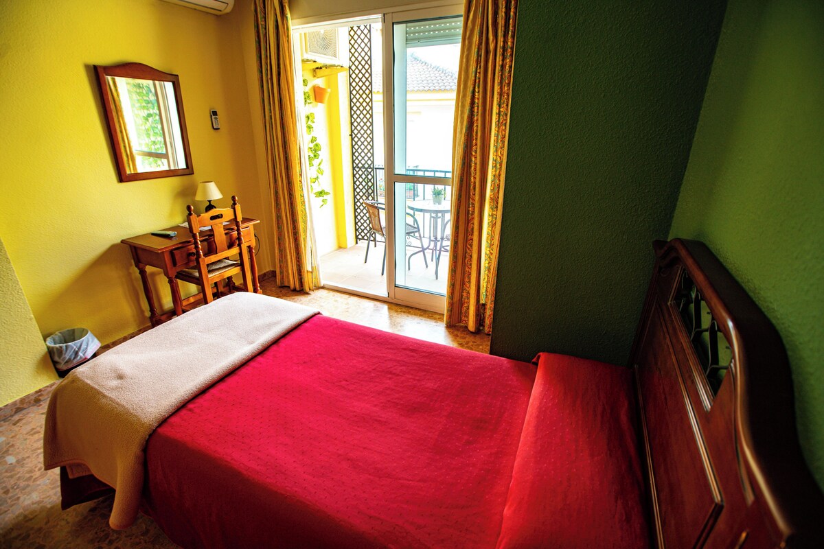 Ein Hotelzimmer mit einem Bett, einem Schreibtisch, einem Stuhl und Blick ins Freie.