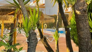 Zona de piscina con palmeras y una estructura de techo de paja.