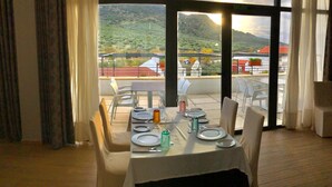 Un comedor con una mesa dispuesta para dos, ventanas amplias con vistas a un paisaje montañoso y un letrero que indica la salida.