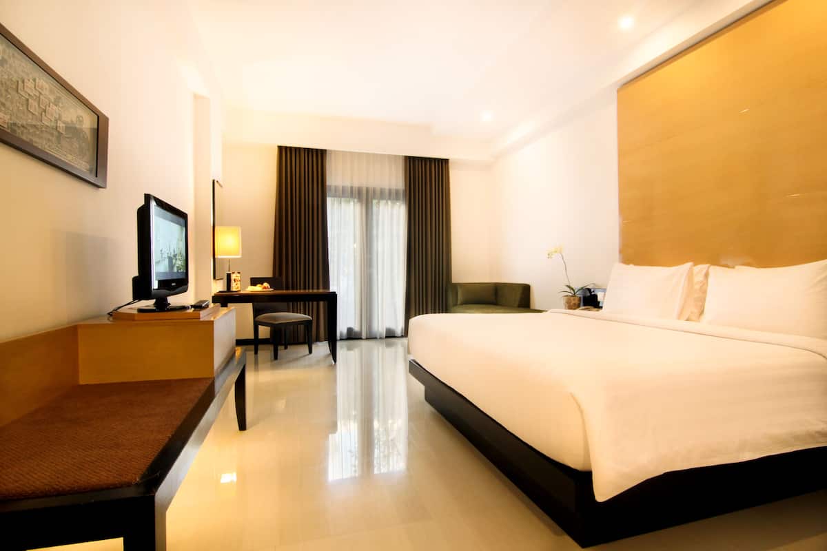 Ein Hotelzimmer mit einem großen Bett, einem Schreibtisch mit Computer, einem Sessel und einem Fernseher.