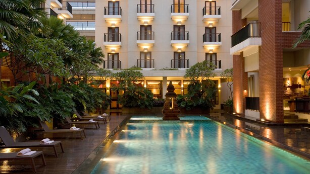 A hotel with a swimming pool, lounge chairs, and a fountain.