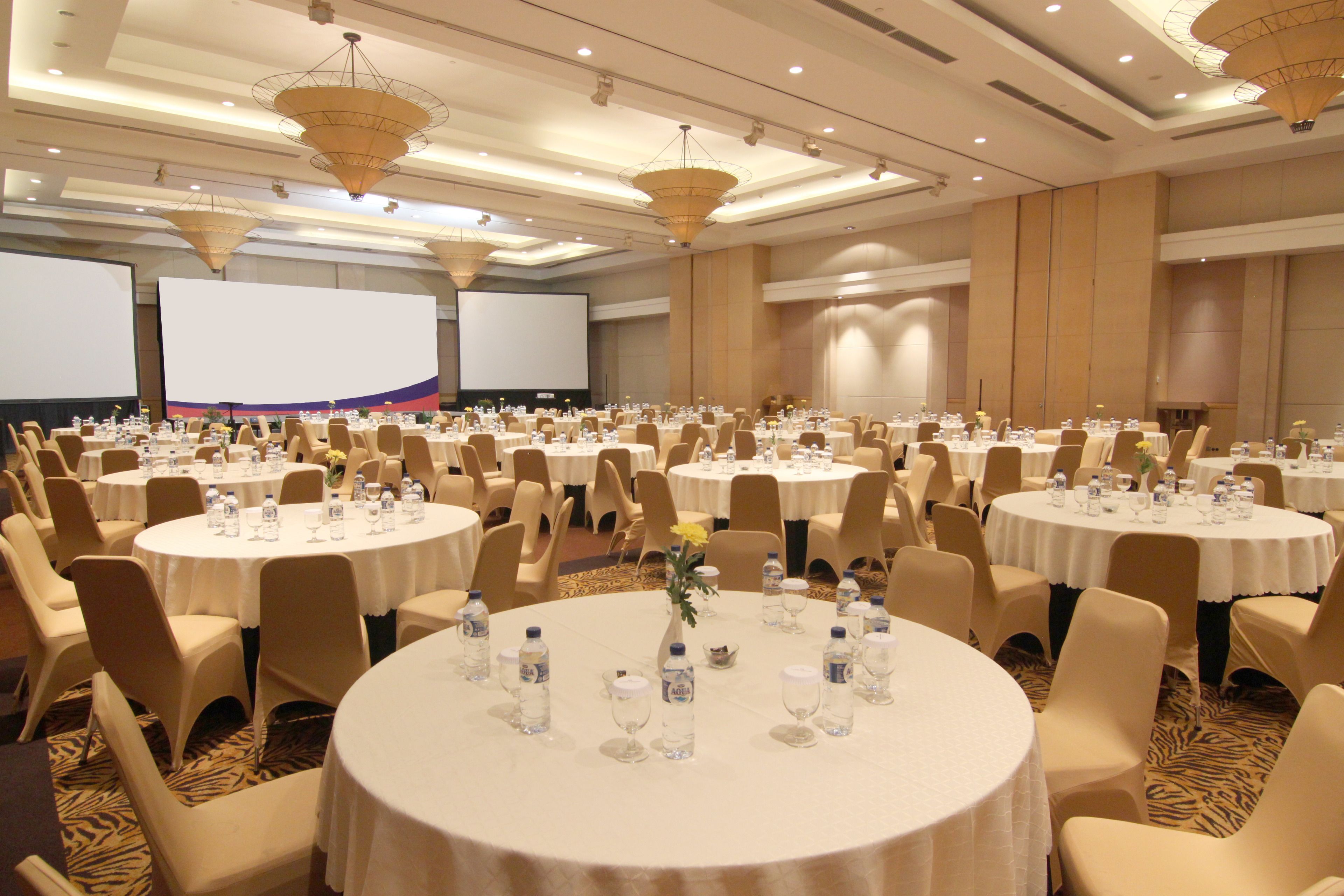 A conference room with multiple round tables, each set with water bottles and glasses, and beige chairs.