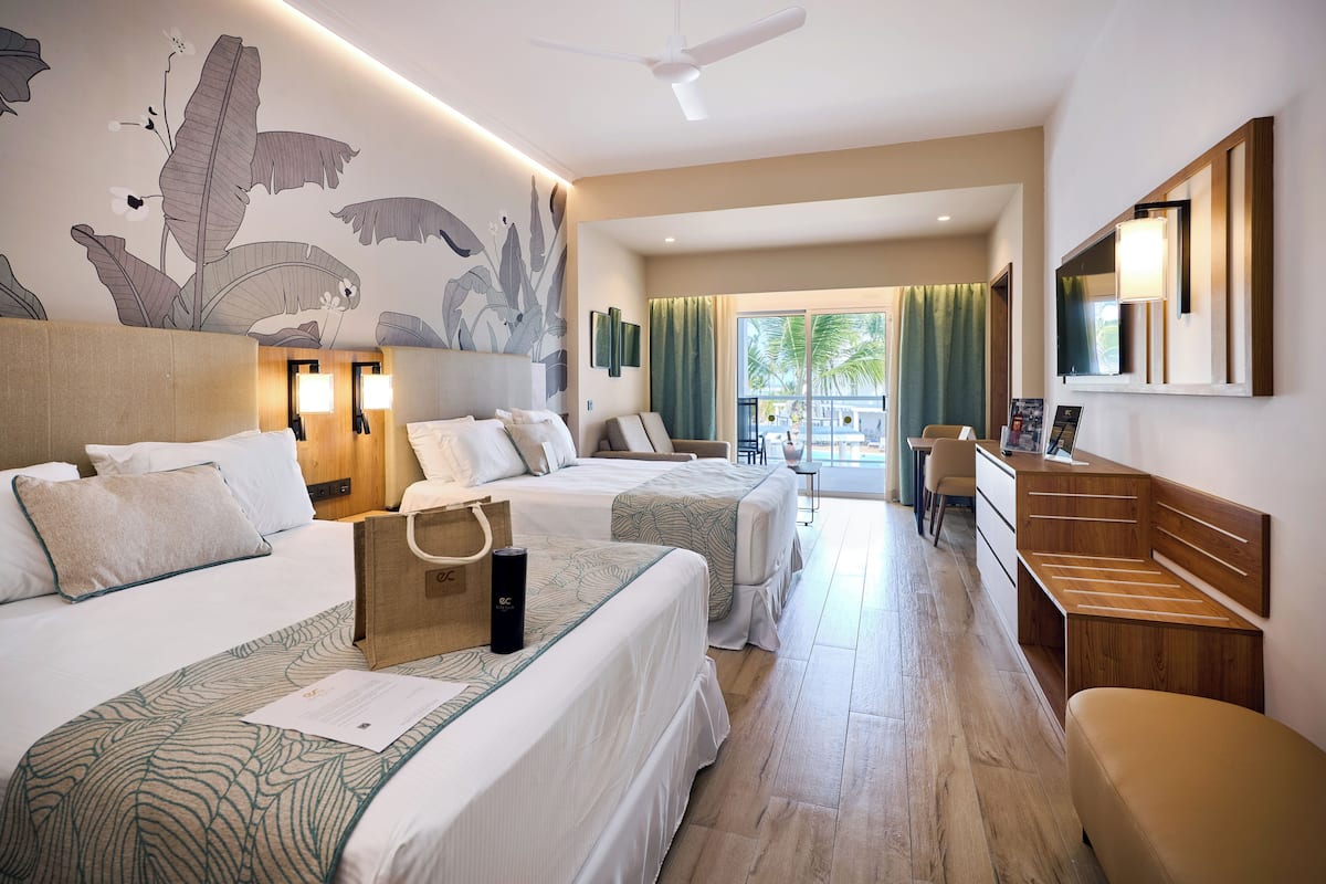 Une chambre d’hôtel avec deux lits, un bureau, une chaise, un grand miroir et une vue sur l’espace extérieur.