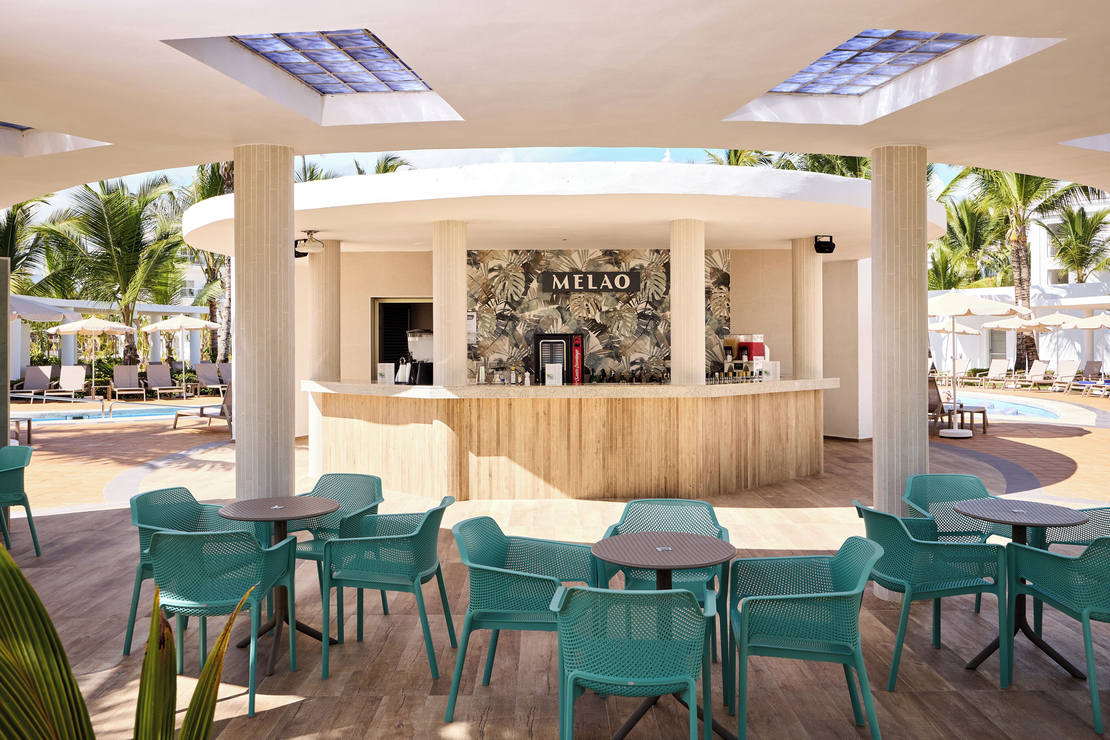 Een bar met een tropische muurschildering, omringd door terrasstoelen en -tafels.