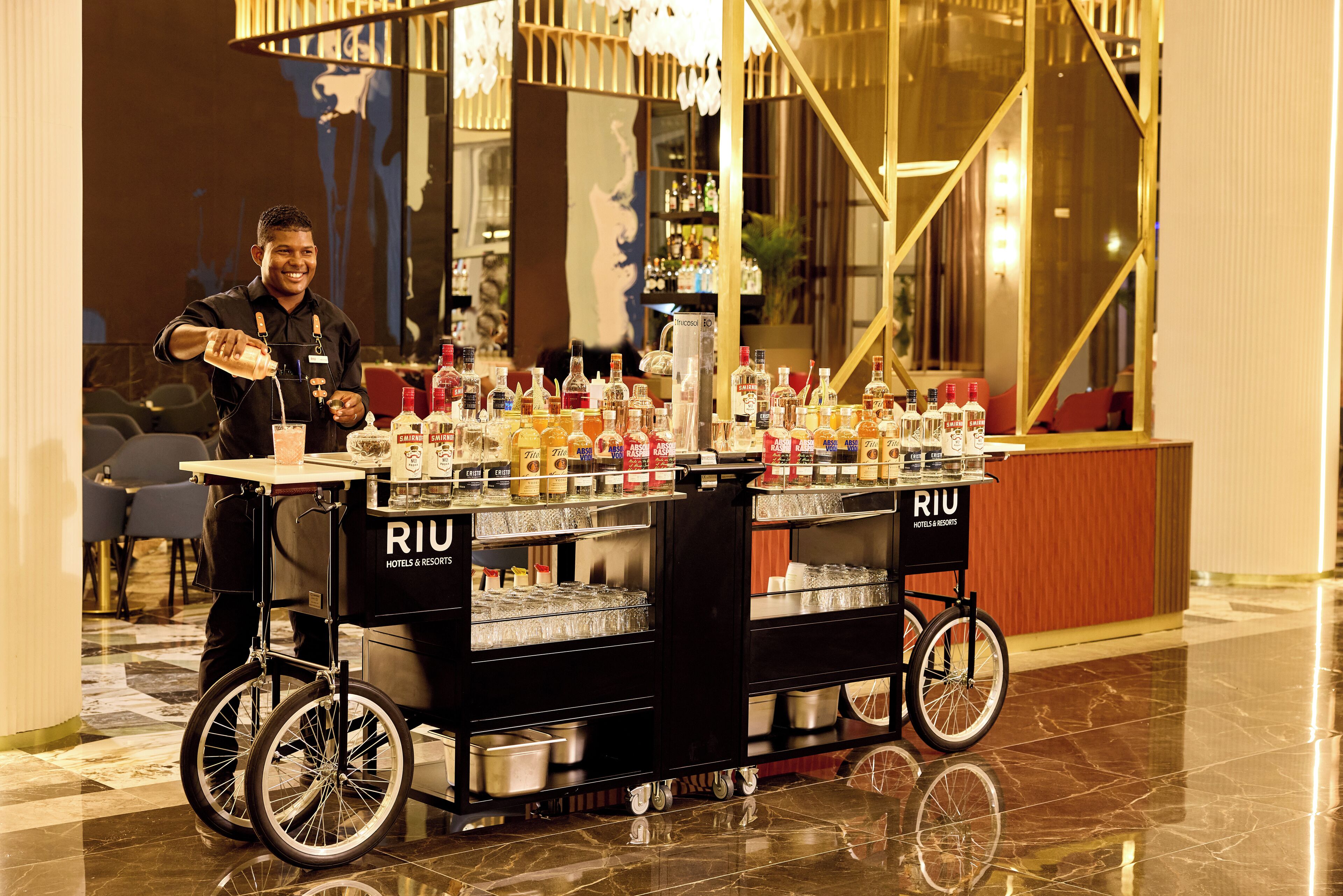Un chariot de boissons contenant plusieurs bouteilles et une pancarte indiquant « RIU Hotels & Resorts ».
