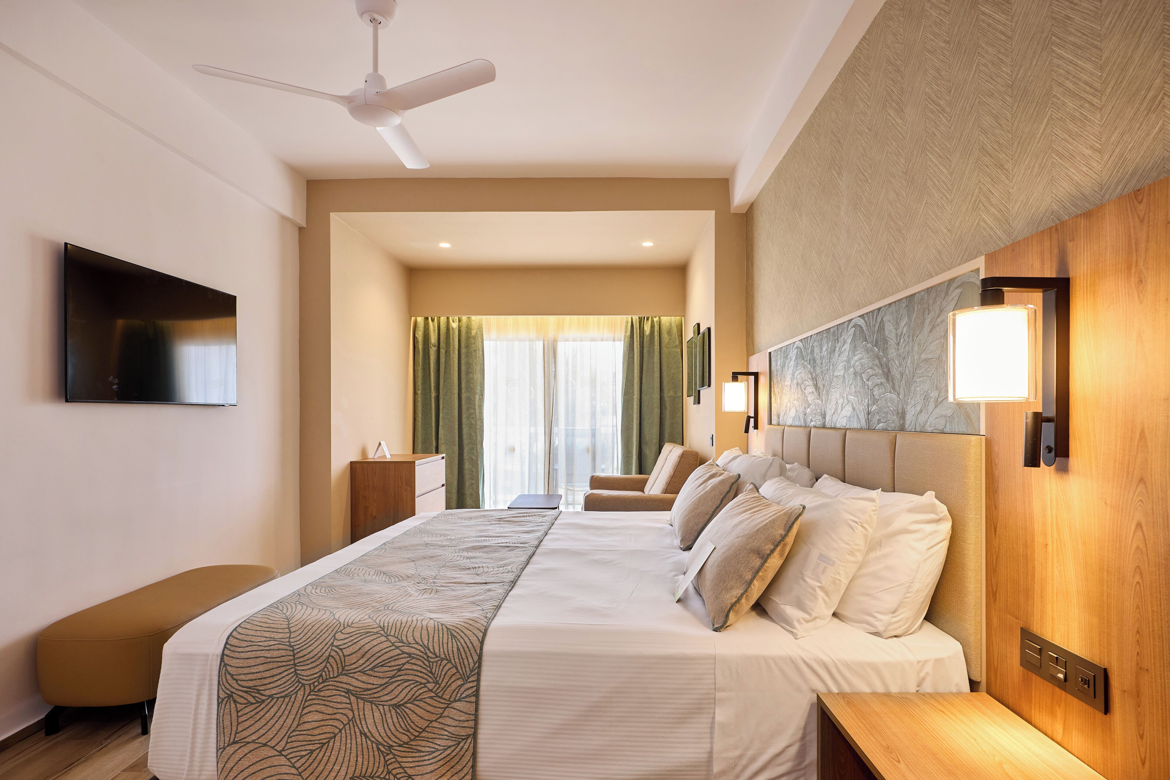 Ein Hotelzimmer mit einem großen Bett, einem Schreibtisch, einem Stuhl, einem Fernseher und einem Deckenventilator.