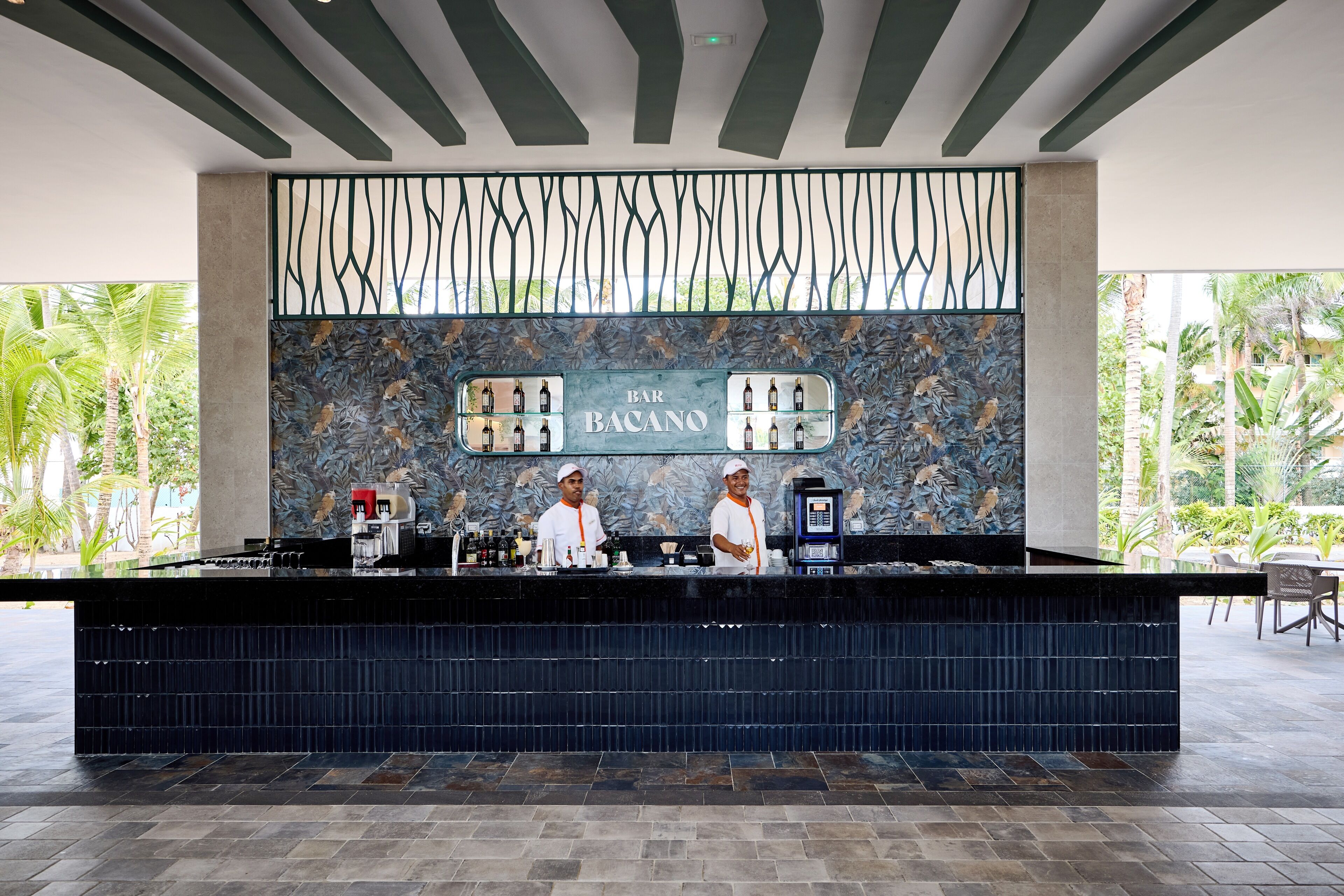 A bar area with a tropical mural, a counter with bar equipment, and two staff members.