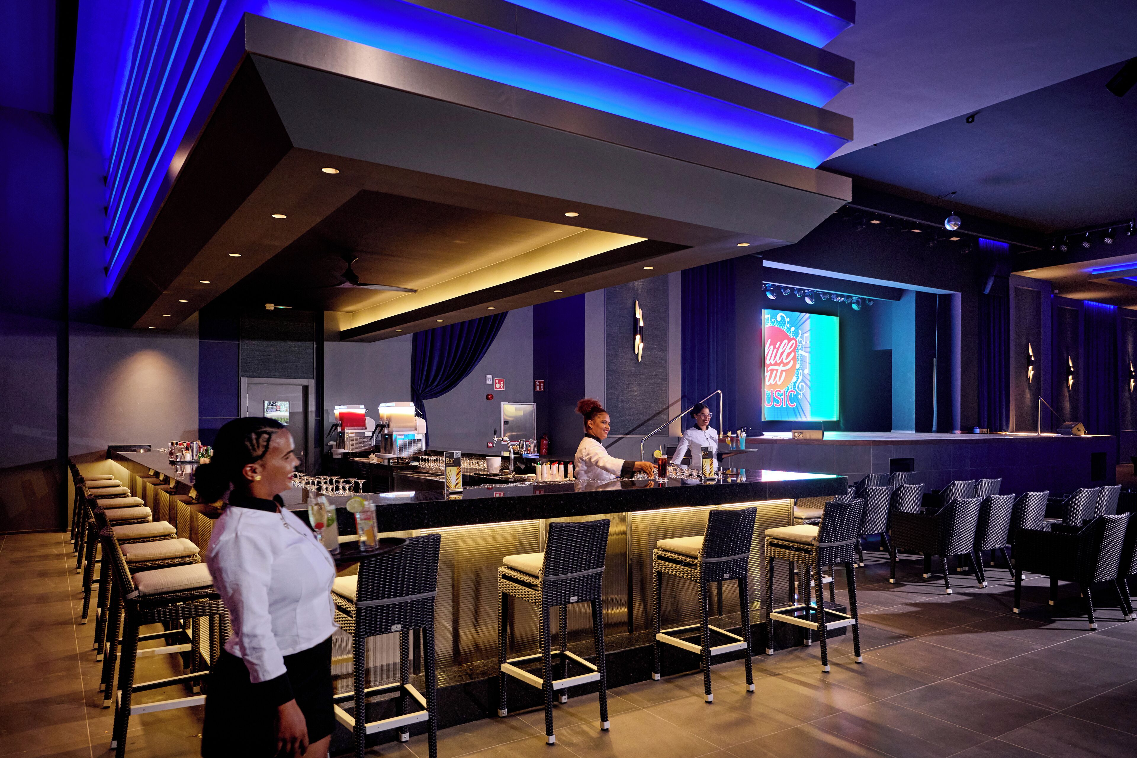 Un espace bar comprenant un comptoir, des tabourets de bar et un coin salon avec des chaises.