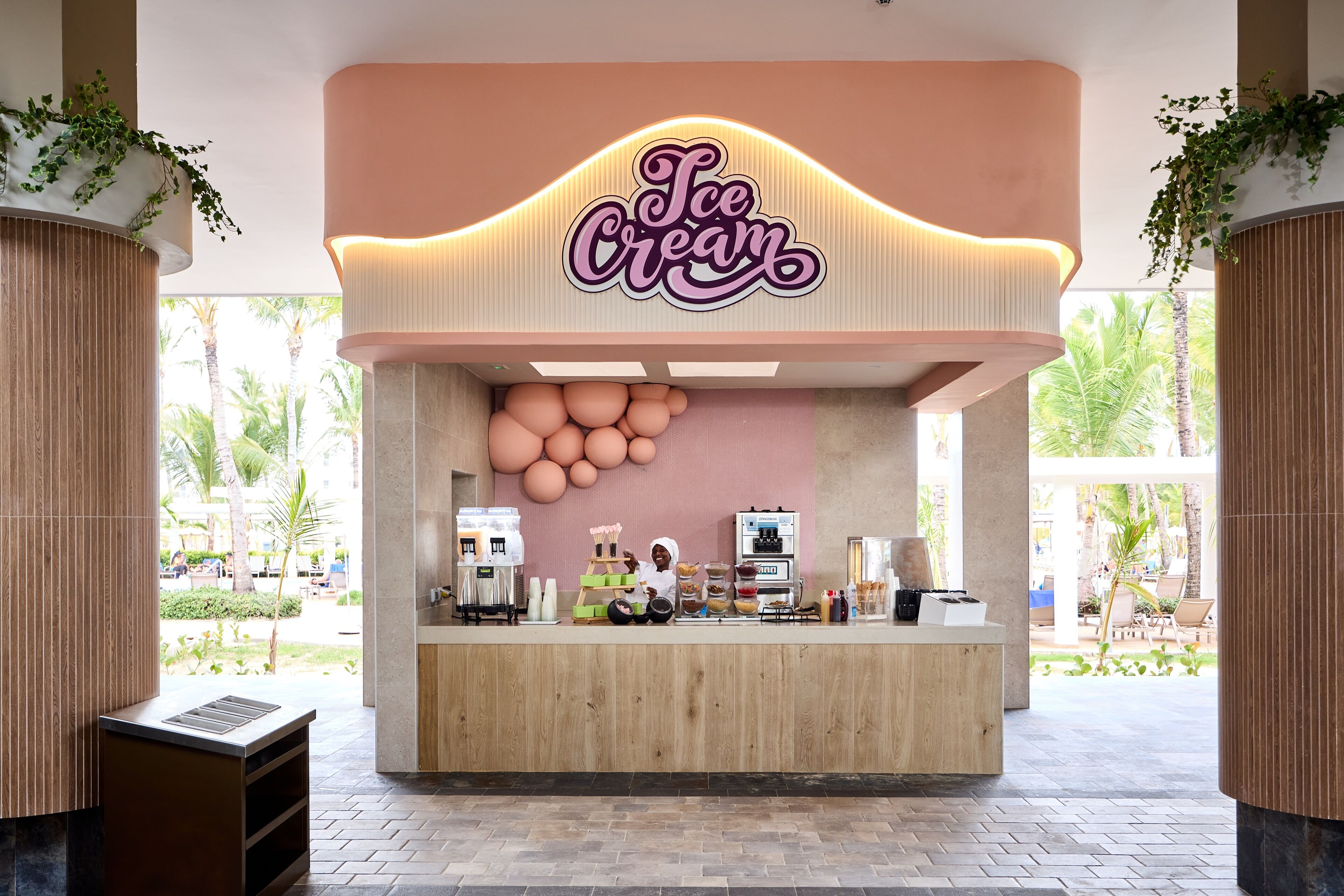 An ice cream shop with a neon sign, a wooden counter, and a view of palm trees outside.