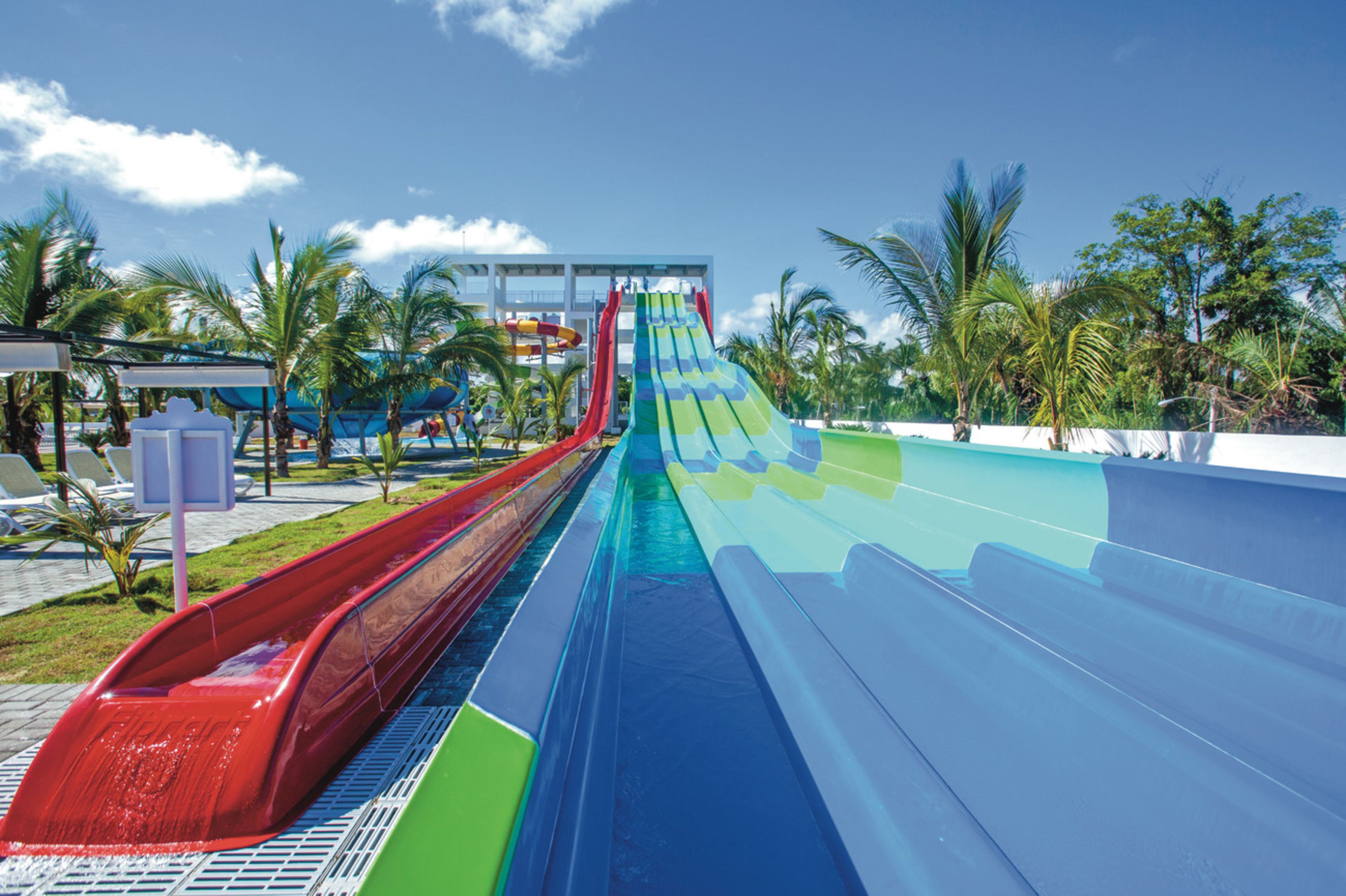 A water park with multiple water slides, palm trees, and a clear blue sky.