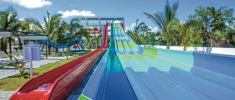 A water park with multiple water slides, palm trees, and a clear blue sky.