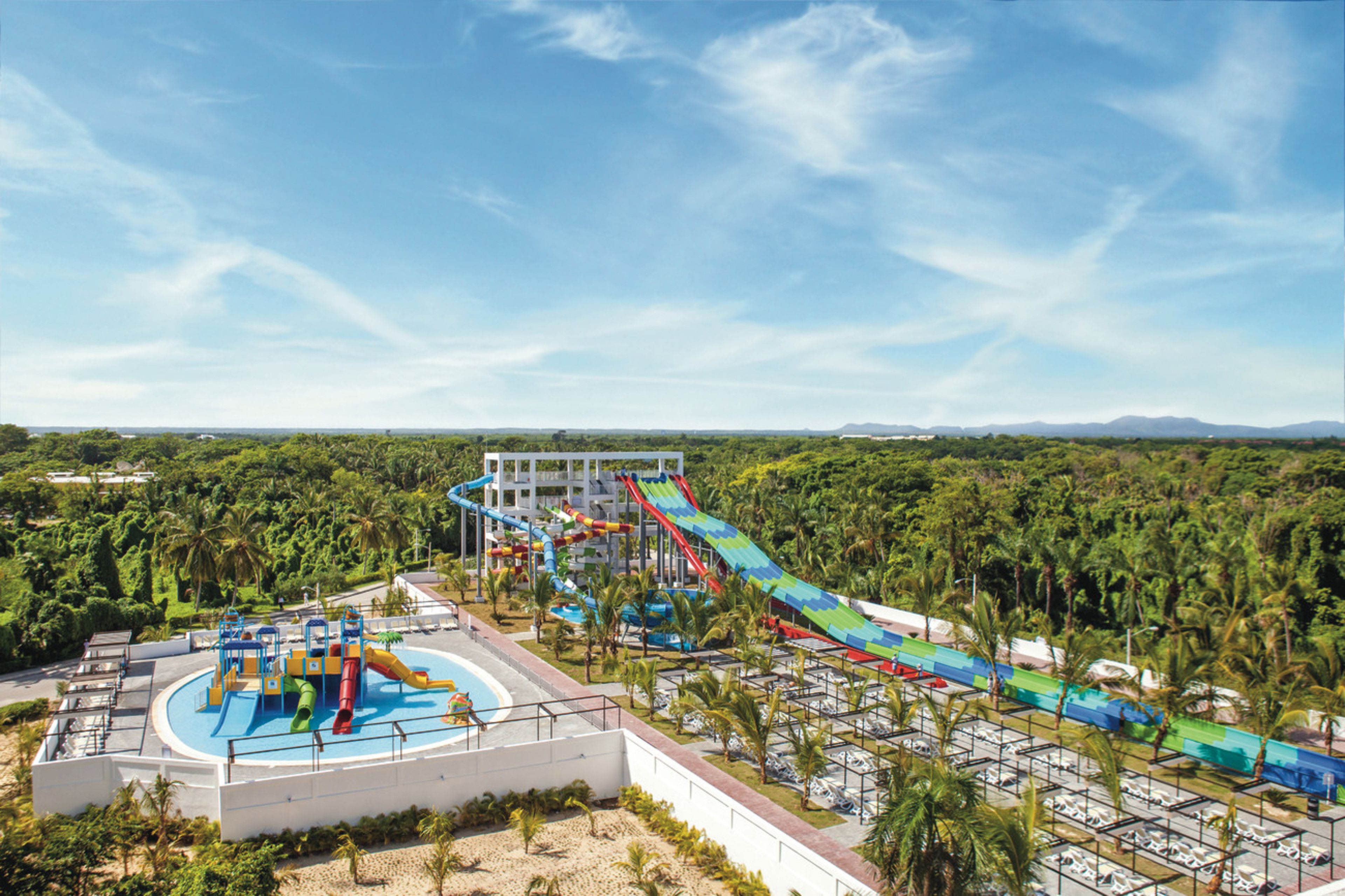 A water park with a large pool, multiple slides, and a parking area surrounded by palm trees.