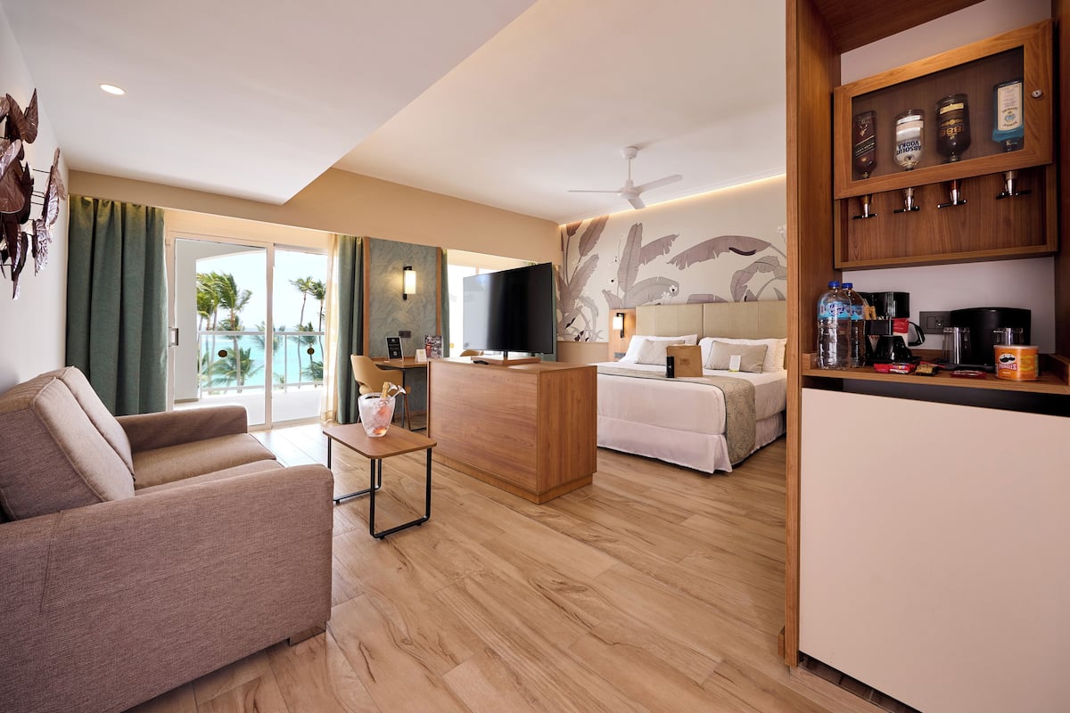 Une chambre d’hôtel moderne équipée d’un canapé, d’un lit, d’une télévision, d’un bureau et d’un coin cuisine avec une machine à café.