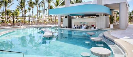 A pool area with lounge chairs, a bar, and palm trees.