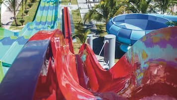 A water slide with multiple lanes, surrounded by palm trees and a pool area.