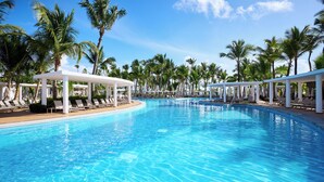 A large, clear swimming pool with lounge chairs and umbrellas, surrounded by palm trees.