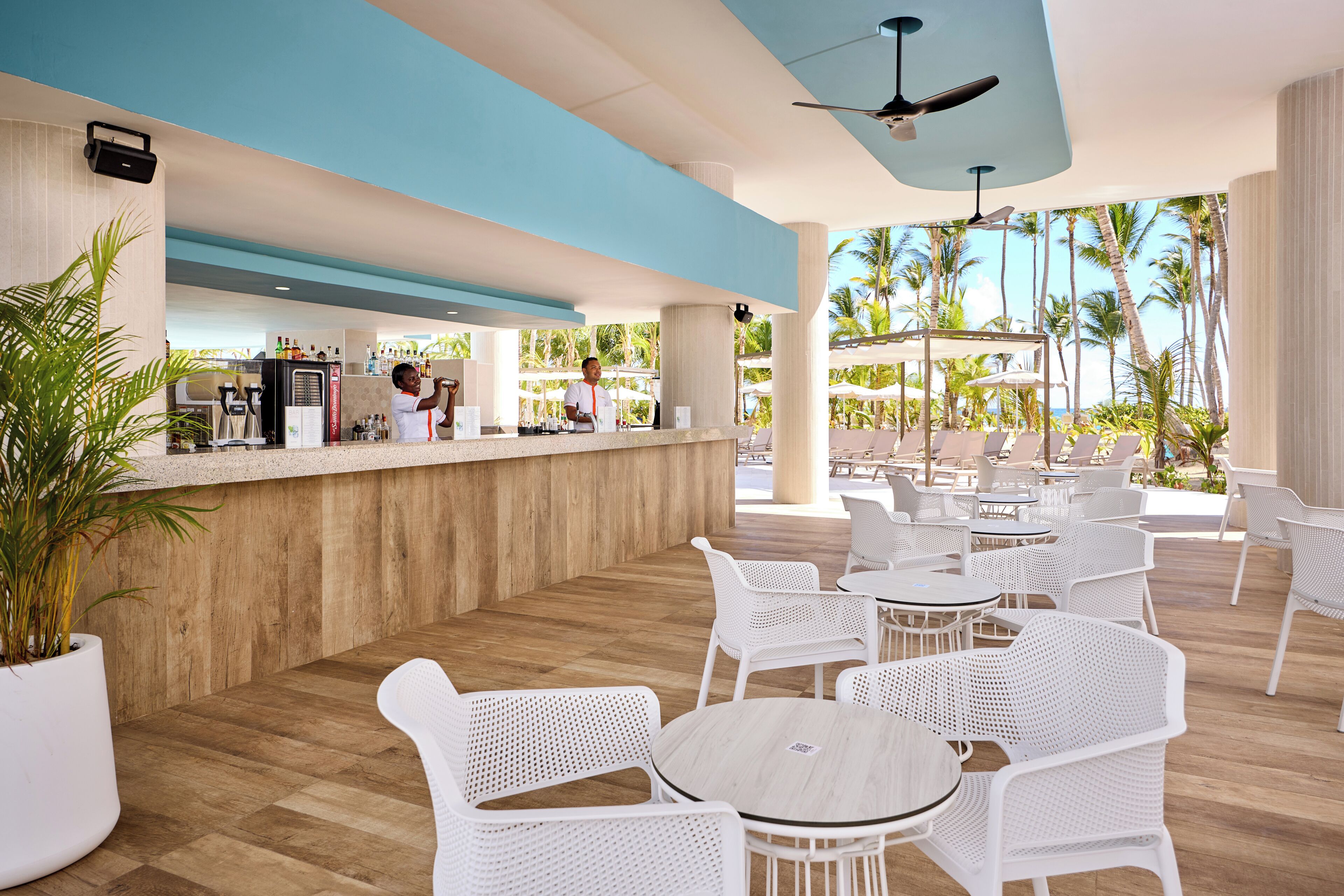 A modern outdoor bar area with a wooden counter, white wicker chairs, and tables.