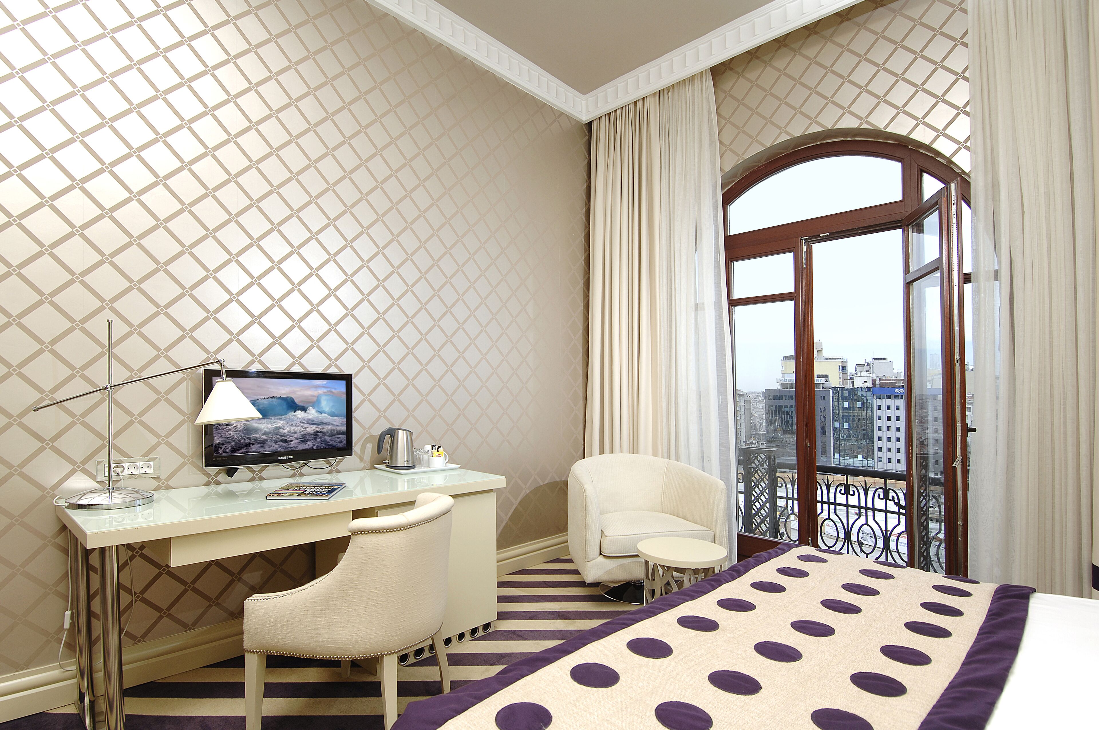 A hotel room with a desk, chair, and a bed with a polka dot bedspread.