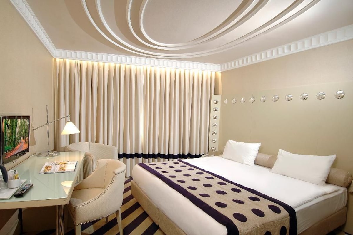 A hotel room with a bed, a desk, a chair, a television, and a wall with circular decorations.
