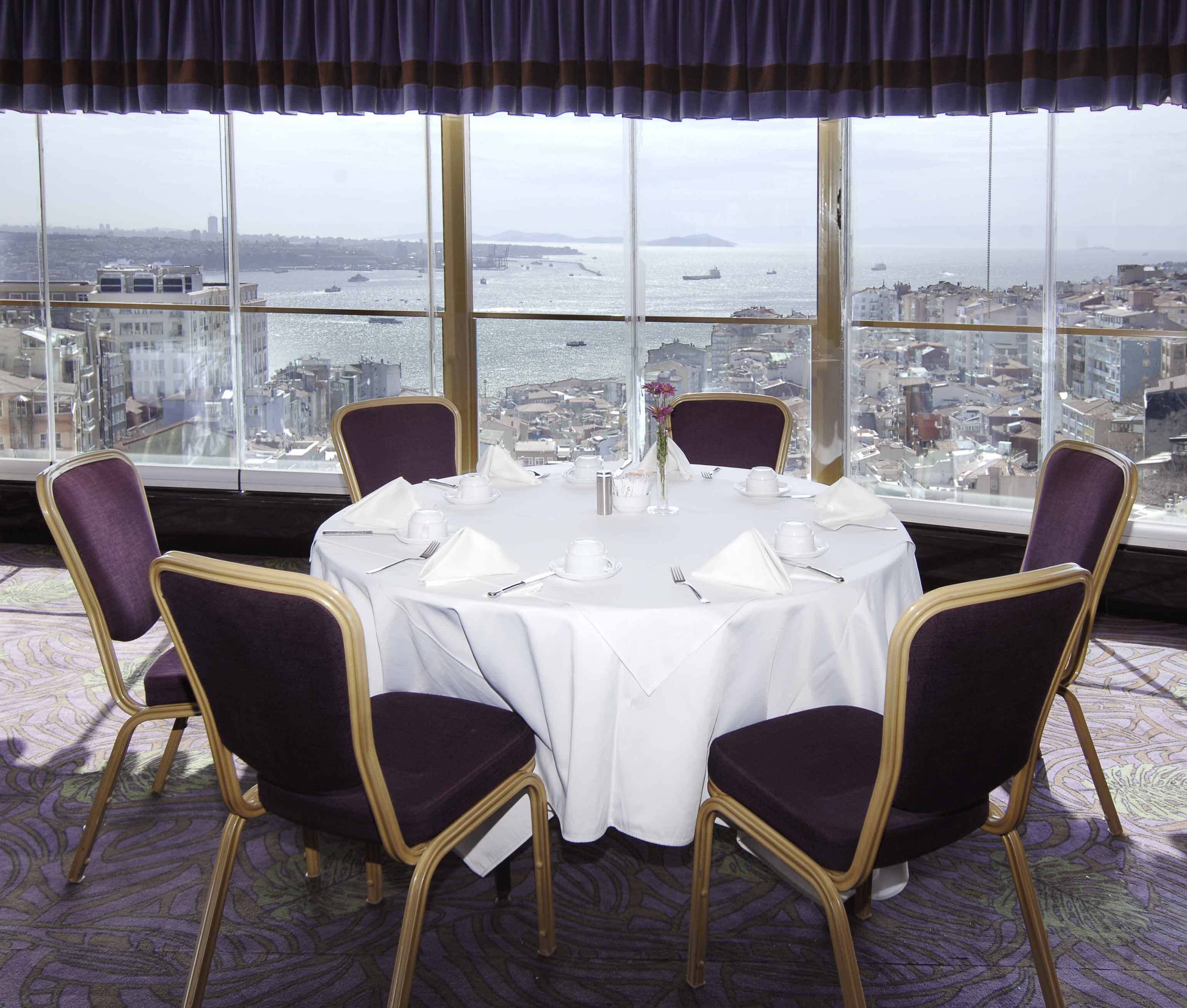 A dining table set for six with chairs, a view of a cityscape and water through large windows.