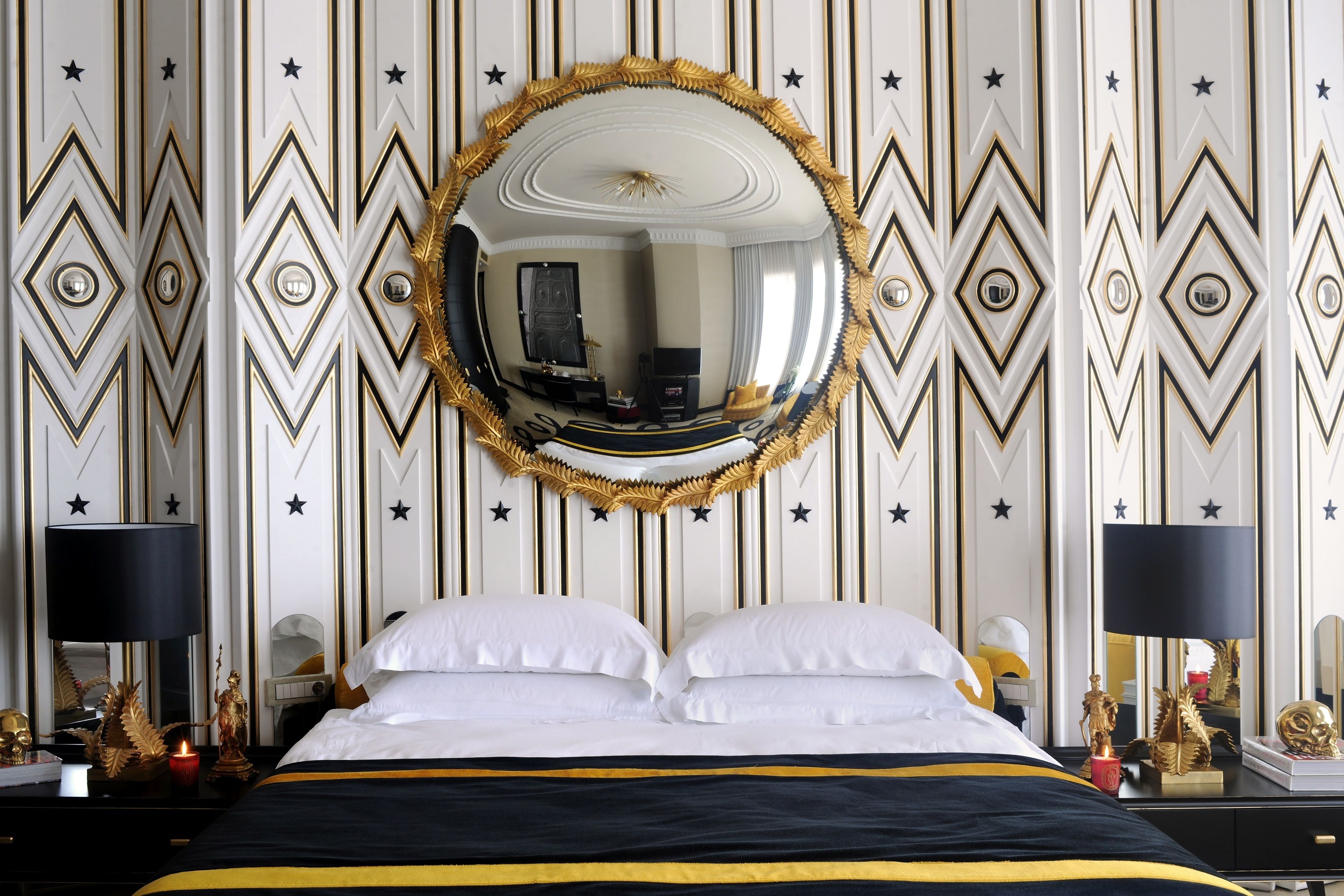 Une chambre d’hôtel avec un grand lit, un miroir rond et un mur décoratif orné de motifs en forme d’étoiles.