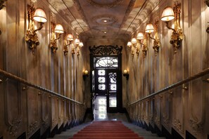 A grand staircase with ornate wall sconces and a decorative ceiling, leading to a black-framed door. - Taxim Hill Hotel (Istanbul)