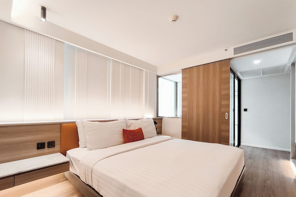 A modern hotel room with a large bed, wooden headboard, and a built-in bench.