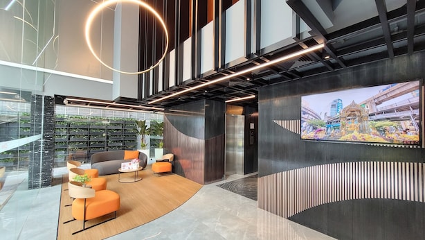 A modern interior with a curved seating area, a large TV screen, and a wall-mounted shelf with plants. - Citrus Sukhumvit 13 Nana Bangkok by Compass Hospitality (Bangkok)