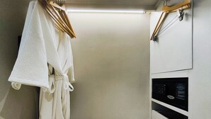 A walk-in closet with a wooden floor, a white robe hanging on a wooden hanger, and a black appliance on the right wall. - Citrus Sukhumvit 13 Nana Bangkok by Compass Hospitality (Bangkok)