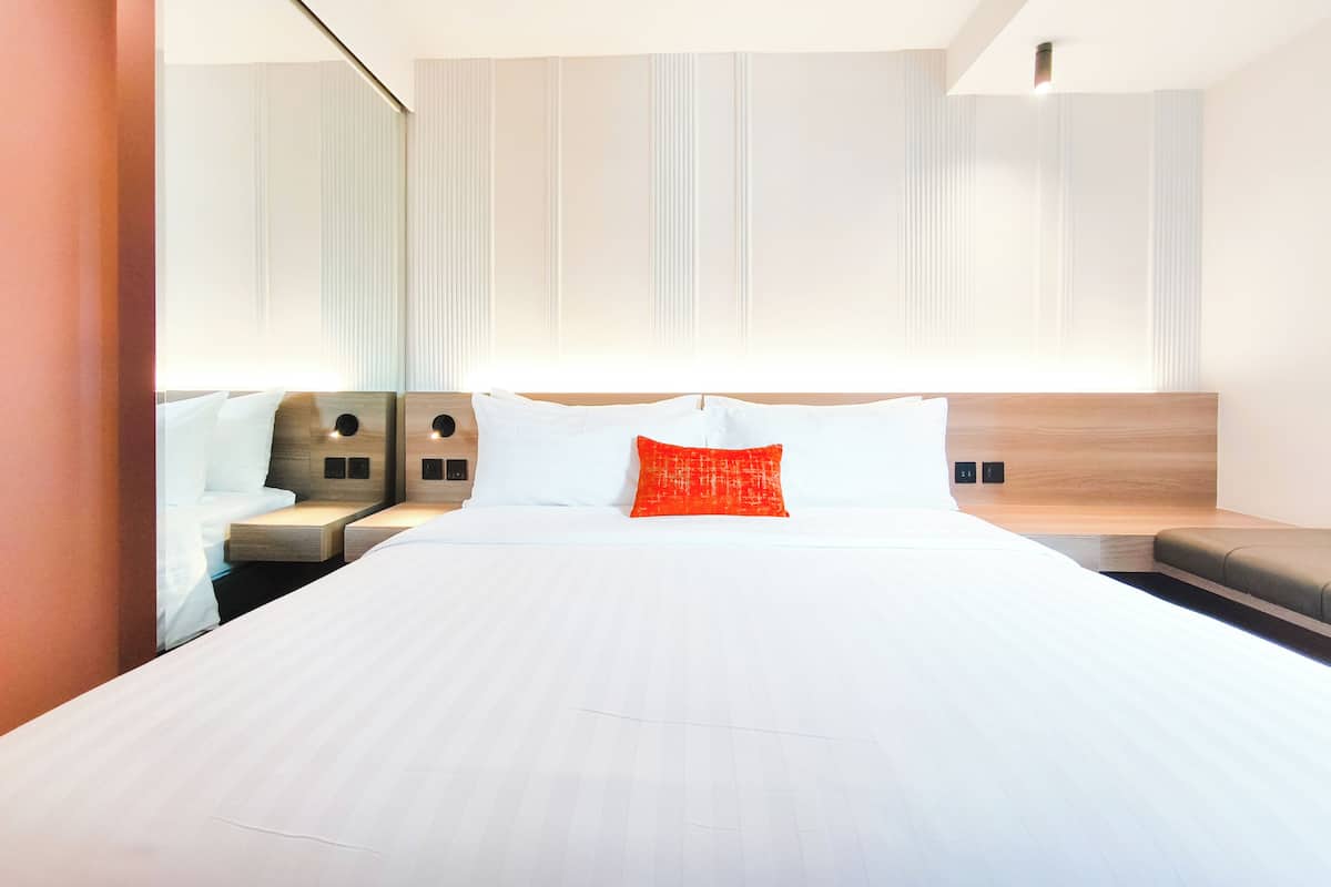 A modern hotel room with a large bed, two bedside tables, and a built-in bench.