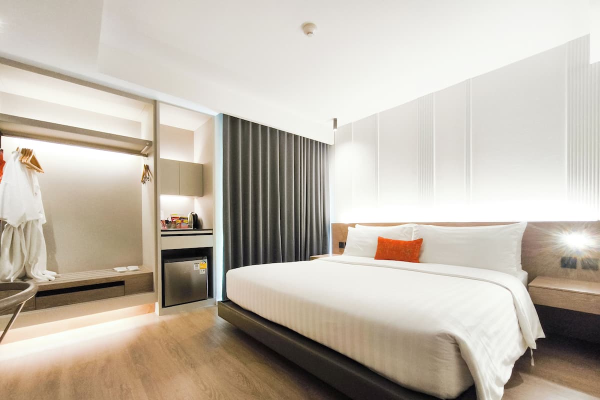 A modern hotel room with a large bed, a small desk, a mirror, and a wardrobe.