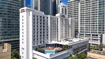 Un hotel di grandi dimensioni con numerosi piani, un'area piscina sul tetto e un cartello ben visibile con la scritta 'Hampton Inn & Suites'.