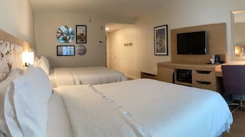 Une chambre d’hôtel avec deux lits, un bureau, une chaise, une télévision et des œuvres d’art accrochées aux murs.