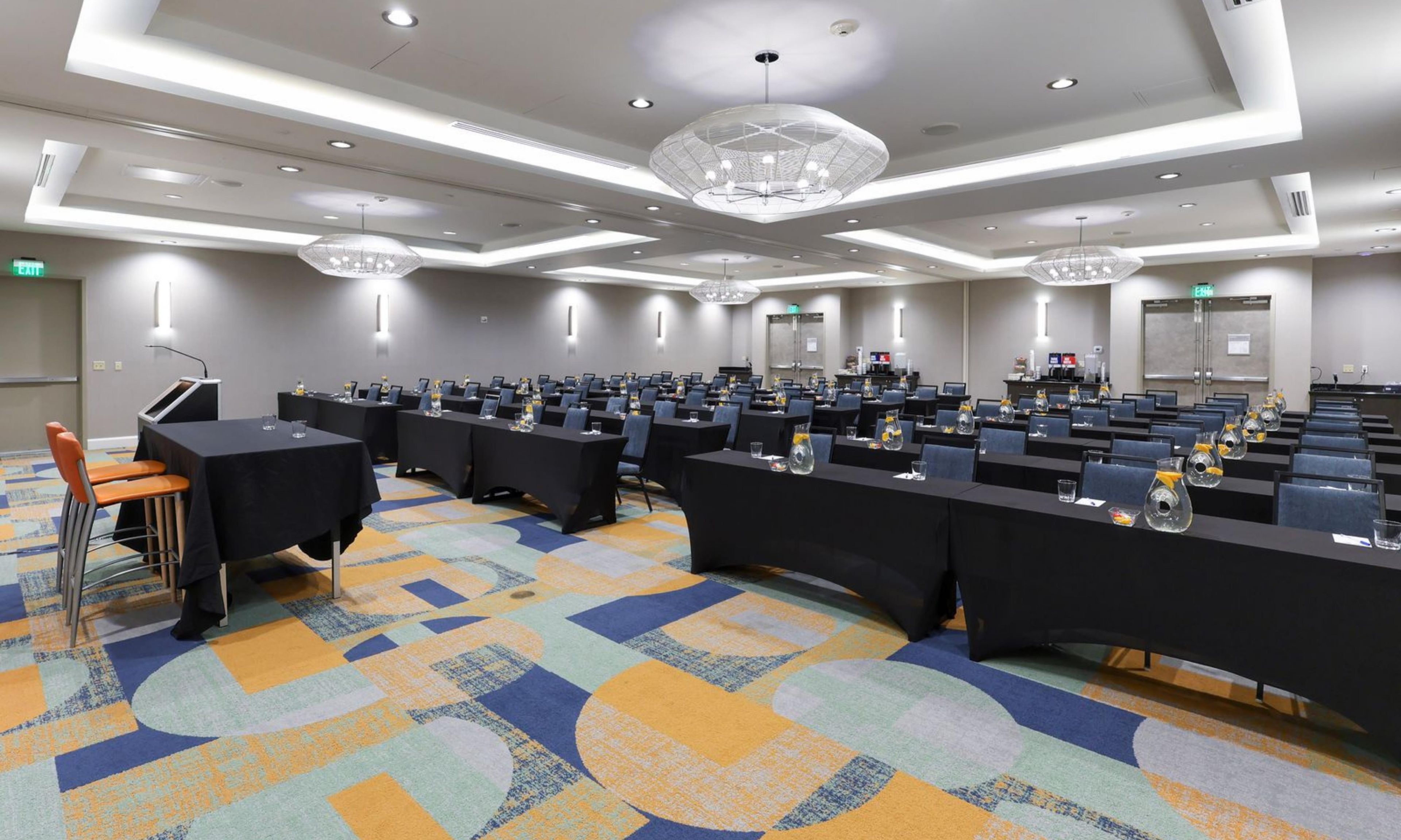 A conference room with multiple tables, chairs, and a patterned carpet.