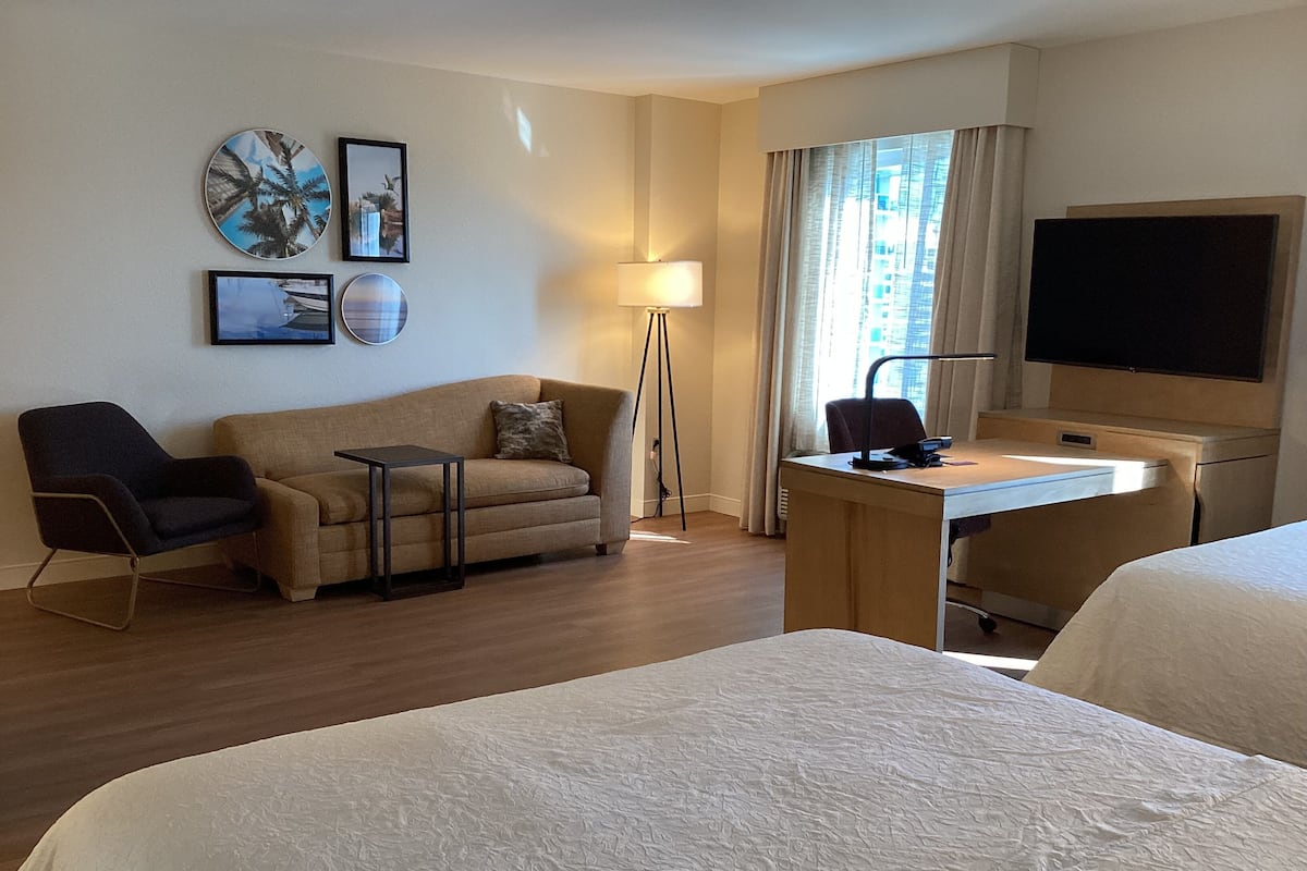 A hotel room with a bed, a desk, a chair, a sofa, and a TV.