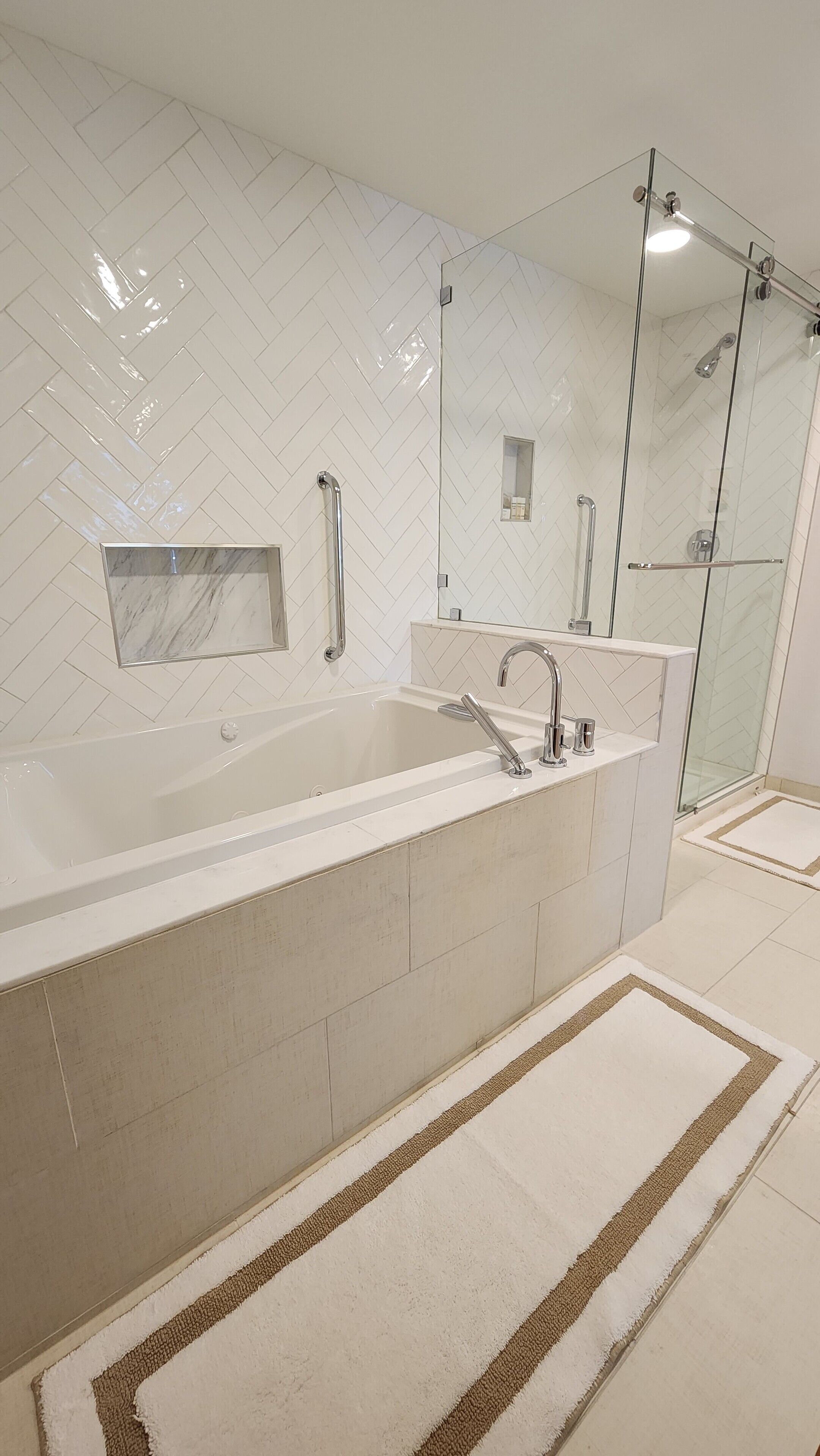 Un baño moderno con una bañera grande, una ducha con cerramiento de vidrio y un revestimiento de pared con diseño de espiga.