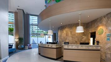 Een hotel receptie met twee balies, een groot raam met uitzicht op gebouwen, en een stenen muur.