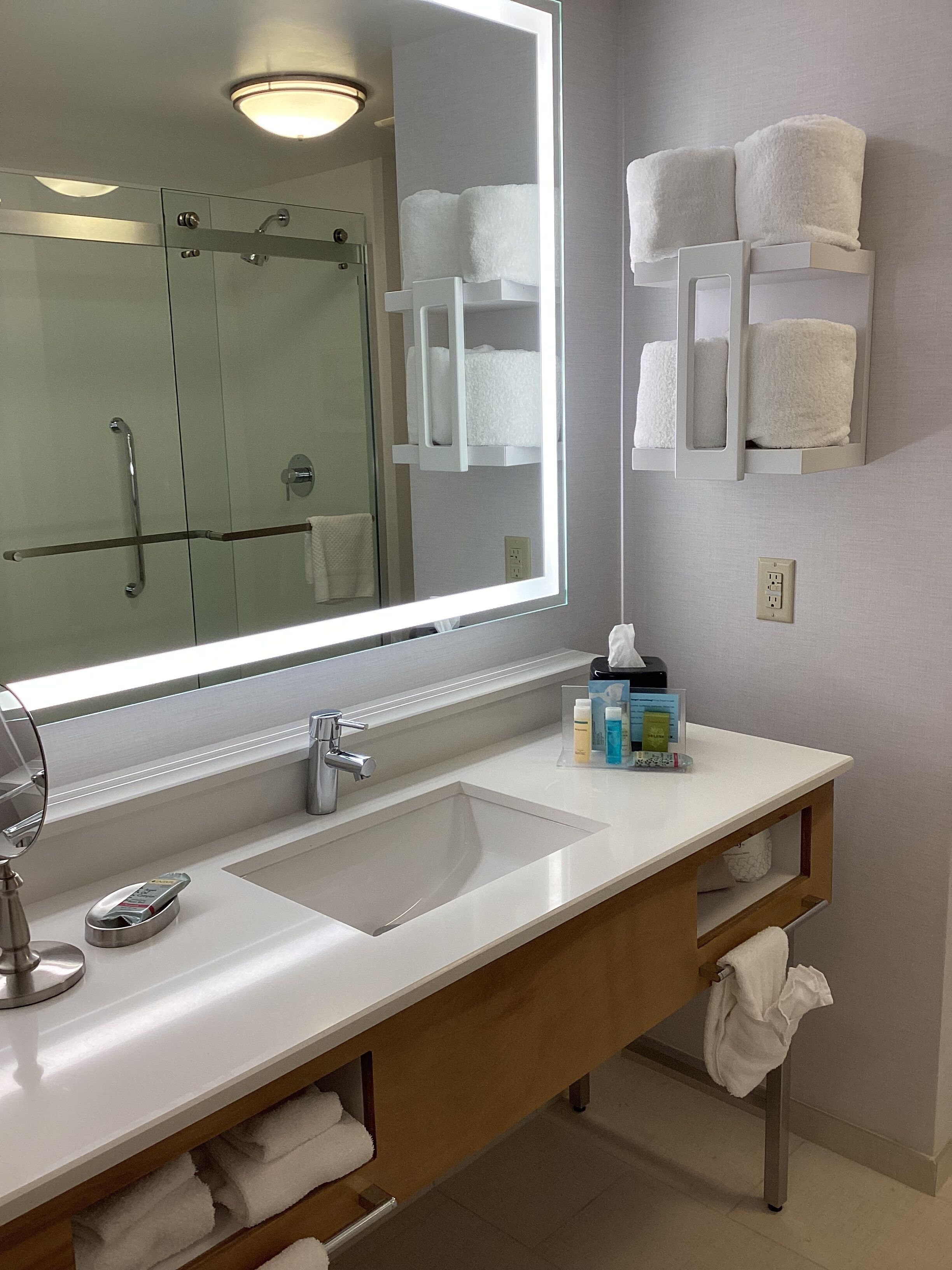 A modern bathroom with a large mirror, two sinks, a shower, and towel racks.