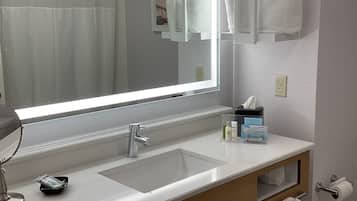 A bathroom with a large mirror, two sinks, a towel rack, and a trash can.