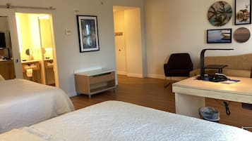 A hotel room with two beds, a desk with a lamp, a chair, and a small table with a phone and papers.