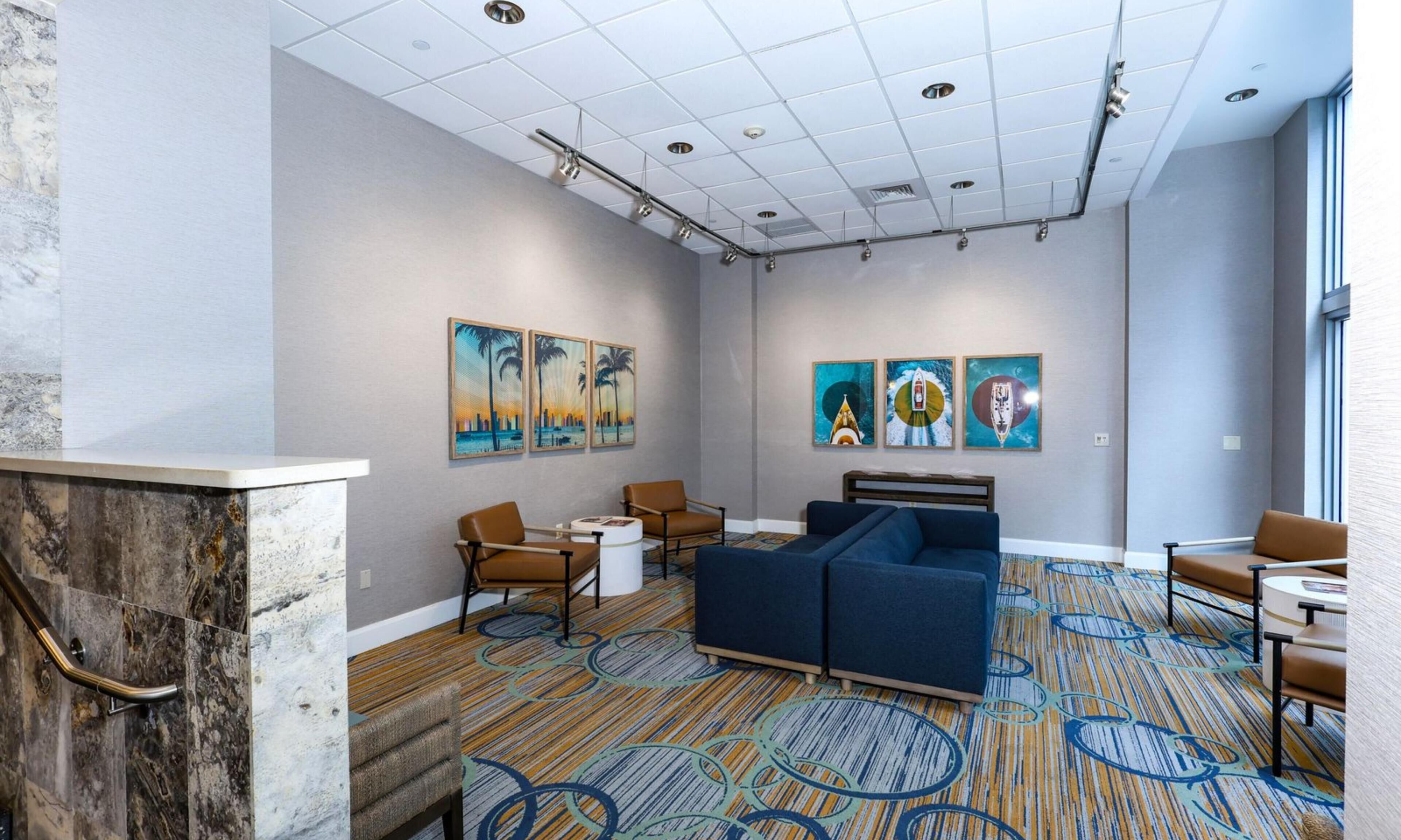 A hotel lobby with a reception desk, seating area, artwork on the walls, and a patterned carpet.