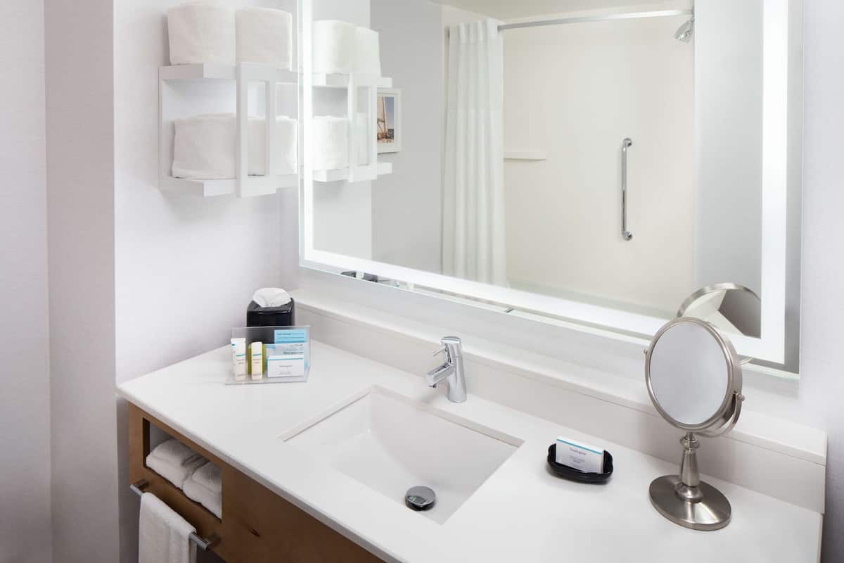 A modern bathroom with a white sink, a large mirror, and a shower visible through the glass door.